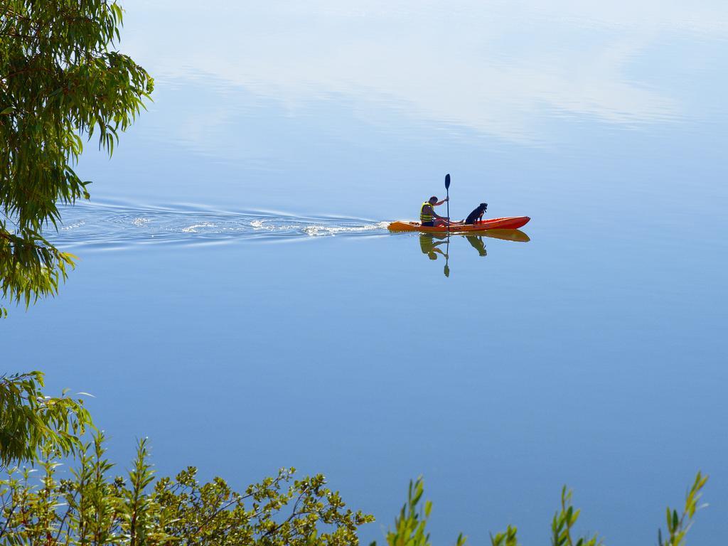 Ap Lago Montargil - Conference & Spa Exterior foto The photo shows a serene scene of a person kayaking on a calm body of water. The surface of the water is very smooth, reflecting the surroundings, and there is a gentle wake behind the kayak indicating movement. The kayaker is wearing a life jacket a