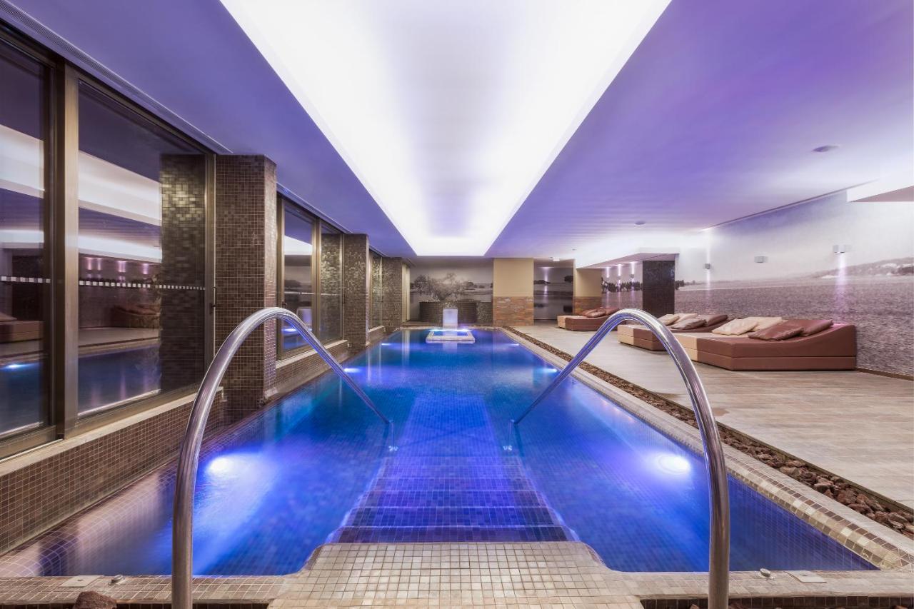 Ap Lago Montargil - Conference & Spa Exterior foto The photo shows a modern indoor swimming pool area. The pool features a sleek design with steps leading into the water and a gentle curve at the sides. The water is illuminated in a blue hue, enhancing the relaxing atmosphere. Surrounding the pool ar