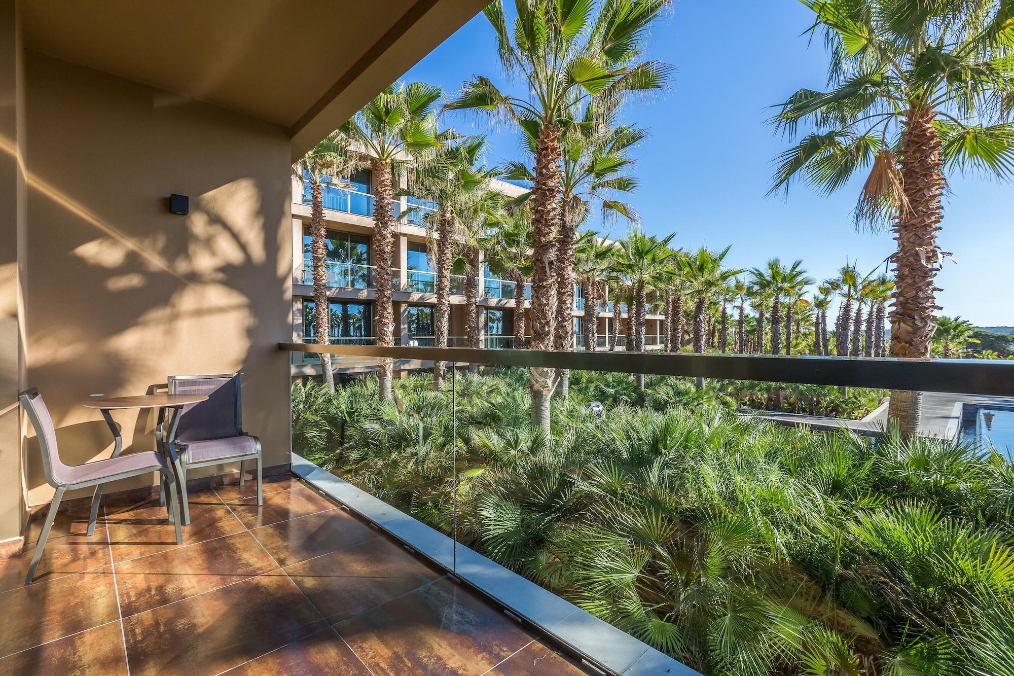 Ap Lago Montargil - Conference & Spa Exterior foto The photo shows a balcony with modern furniture, including a chair and a small table. In the background, there are tall palm trees and lush greenery, suggesting a tropical or resort-like setting. The buildings in the distance are likely part of a hot
