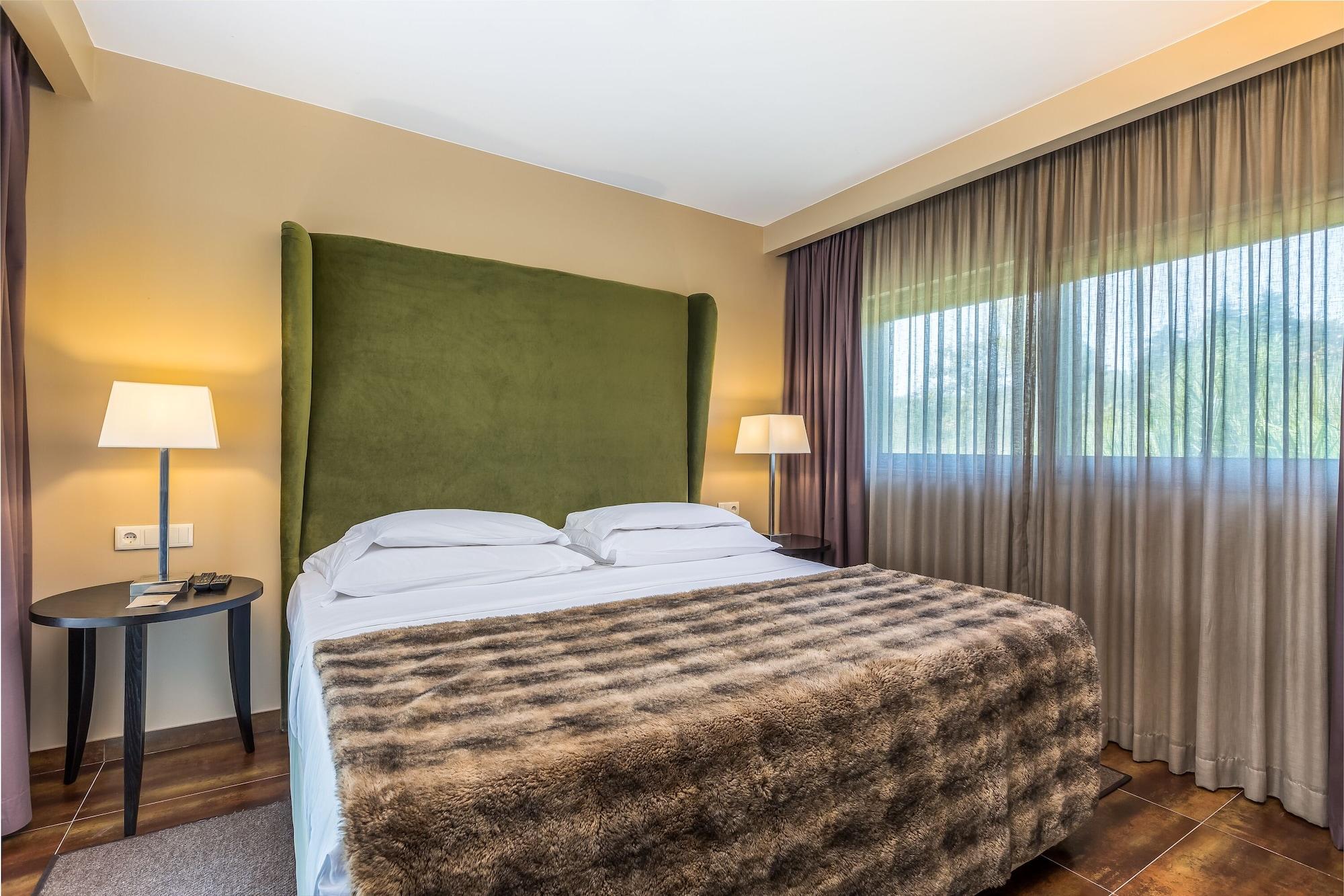 Ap Lago Montargil - Conference & Spa Exterior foto The photo shows a cozy hotel room featuring a large bed with two white pillows and a fur-style blanket draped over it. Behind the bed is a tall, green headboard that adds a touch of color to the room. On either side of the bed are bedside tables, eac