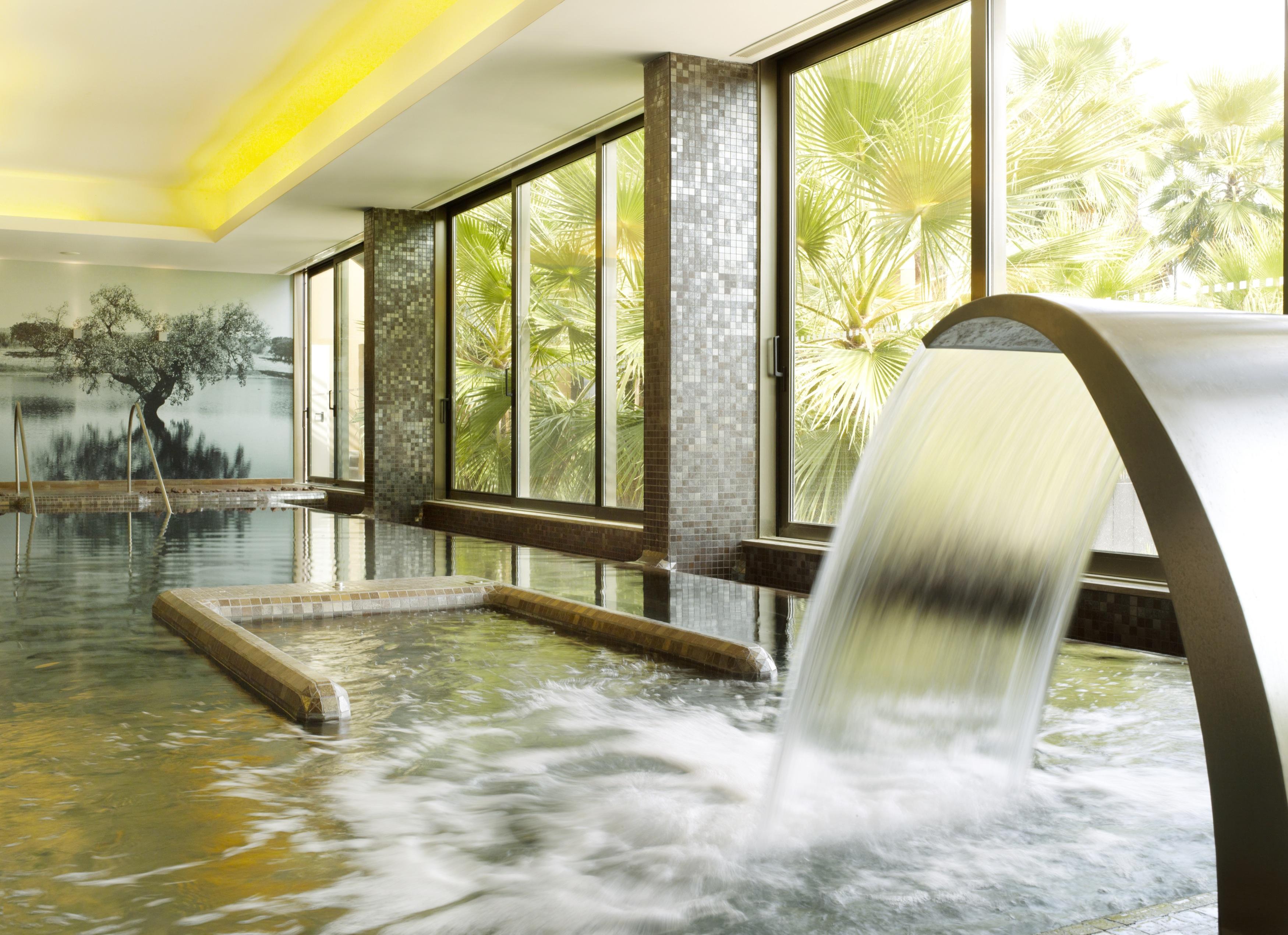 Ap Lago Montargil - Conference & Spa Exterior foto The photo depicts a serene spa environment featuring a tranquil indoor pool area. There is a sleek, modern water feature that spills water gracefully into the pool. Large windows allow natural light to flood the space, showcasing views of lush greene