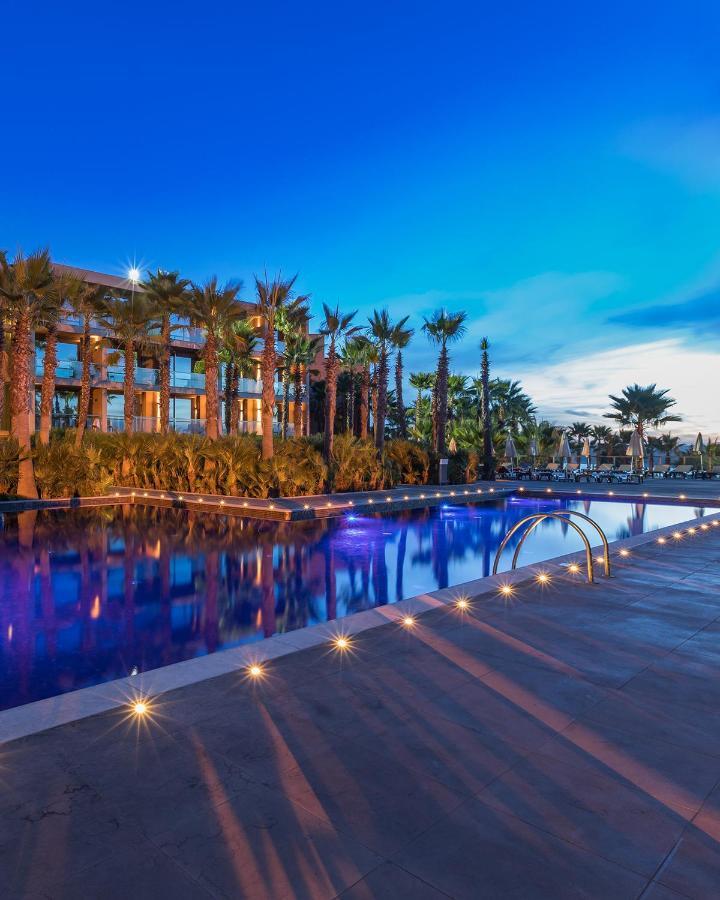 Ap Lago Montargil - Conference & Spa Exterior foto The image shows a serene and inviting outdoor area with a large swimming pool that features a beautiful blue hue, likely illuminated by lights. Surrounding the pool are well-maintained palm trees and lush greenery, creating a tropical atmosphere. In 